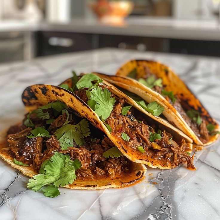 three tacos with meat, cilantro and parsley on a marble countertop