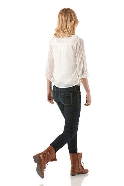 a woman walking with her back turned to the camera and wearing brown boots, jeans and a white blouse