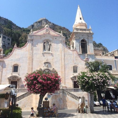 an old church in the middle of town with people sitting on benches and tables around it