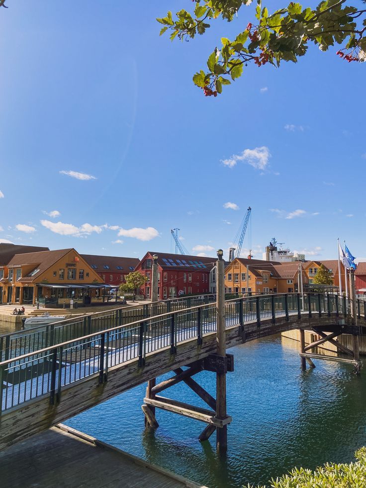 a wooden bridge over a body of water with buildings in the background on a sunny day