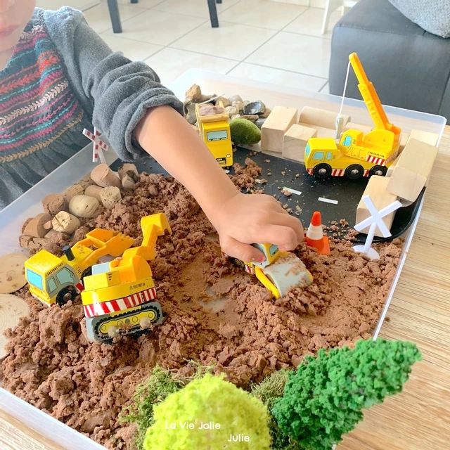 a young boy playing with toys in a play box filled with dirt and construction vehicles