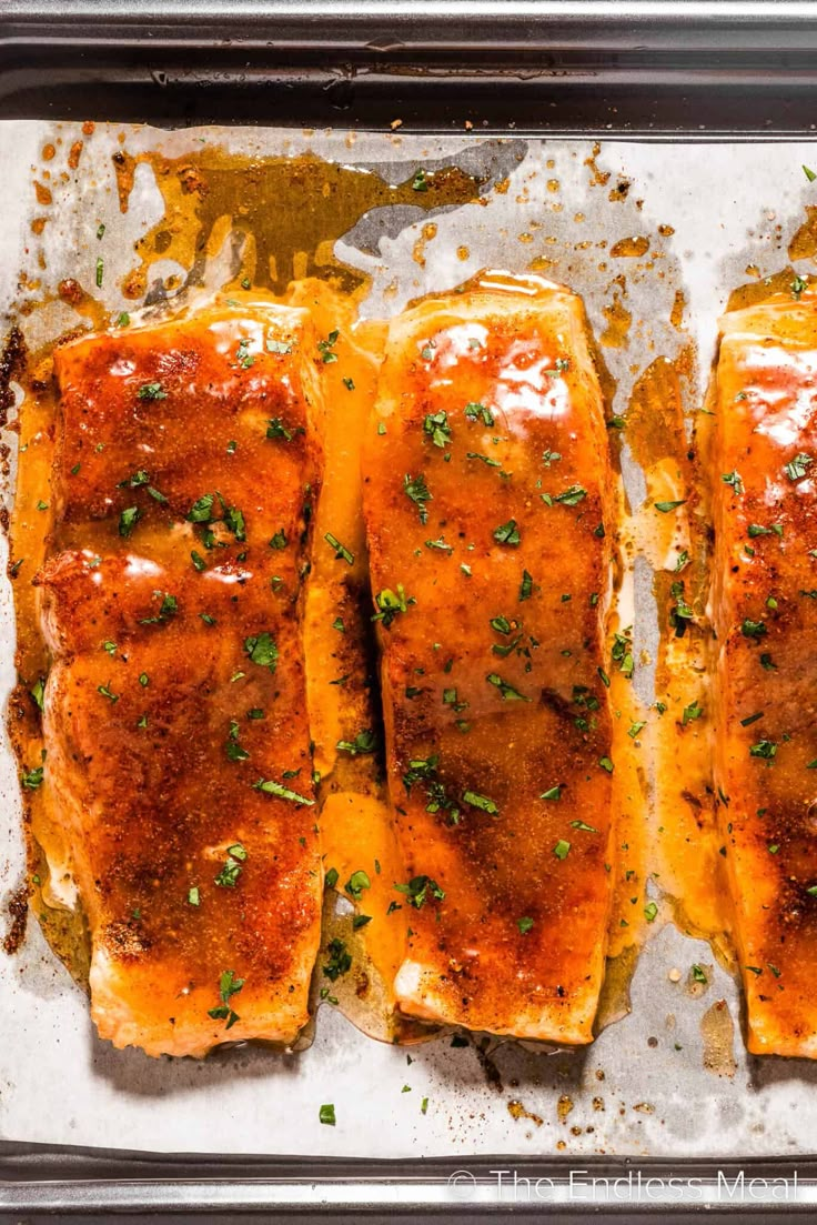 baked salmon fillets in a baking pan with parsley and seasoning sprinkled on top