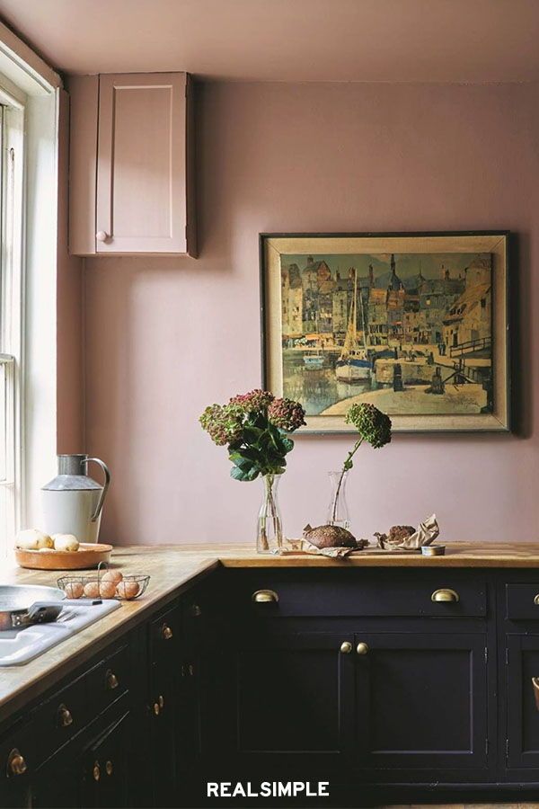 a painting hanging on the wall above a kitchen counter with flowers in a vase next to it