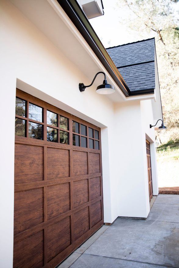 a brown garage door on the side of a white house next to a light pole