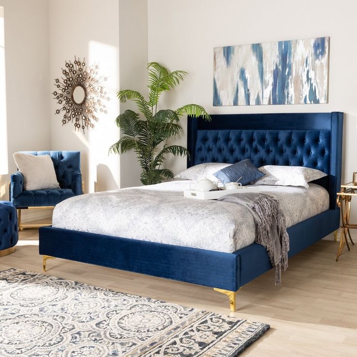 a bed with blue velvet headboard and foot board in a white walled bedroom area