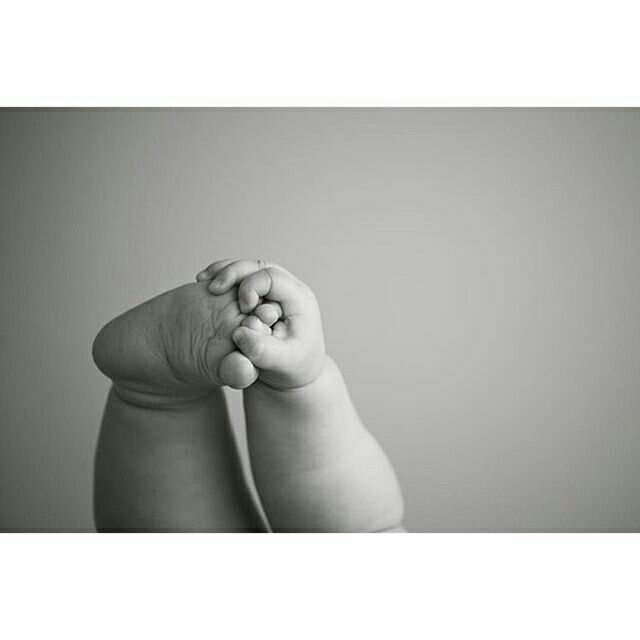 a black and white photo of a baby's hand holding the top of its foot