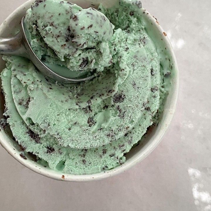 a bowl filled with green ice cream on top of a white counter next to a spoon