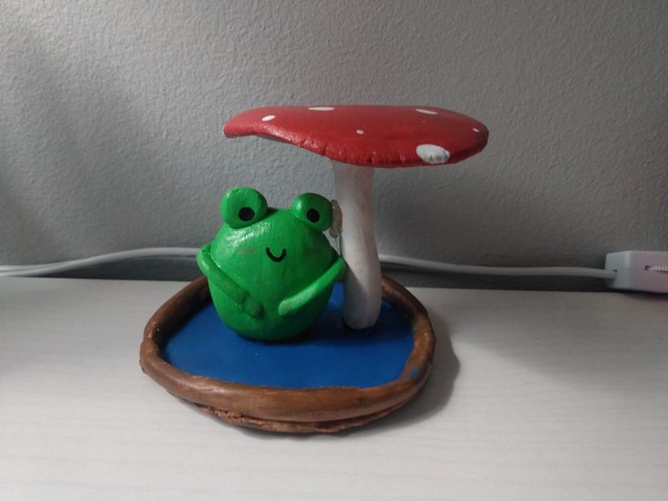 a small green frog sitting on top of a blue tray next to a mushroom shaped object