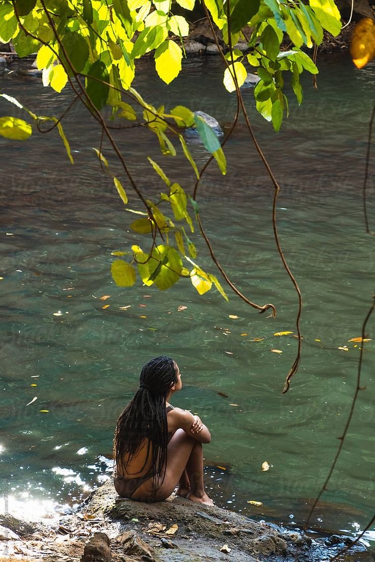 a woman sitting on top of a rock next to a river