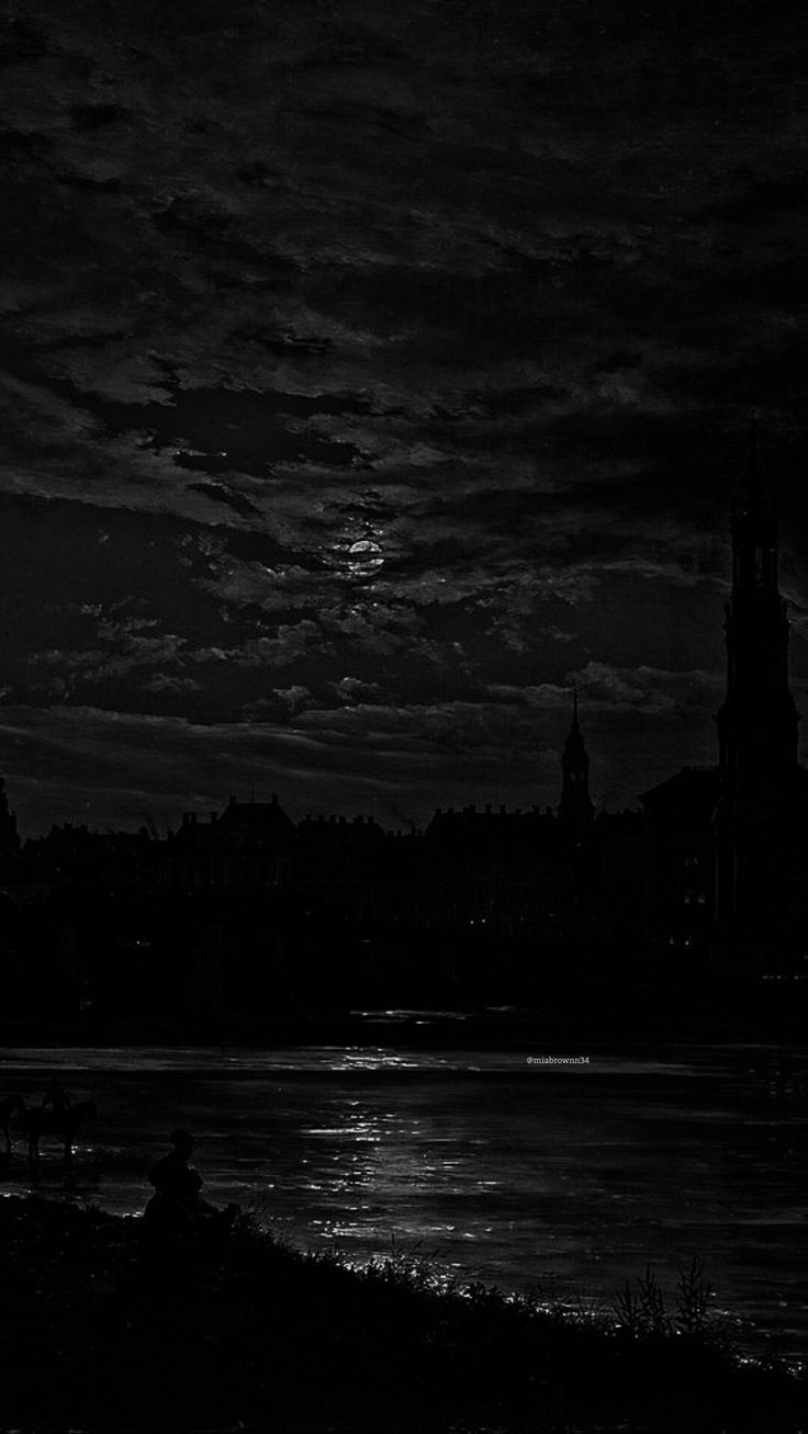 black and white photograph of the moon over a body of water with buildings in the background