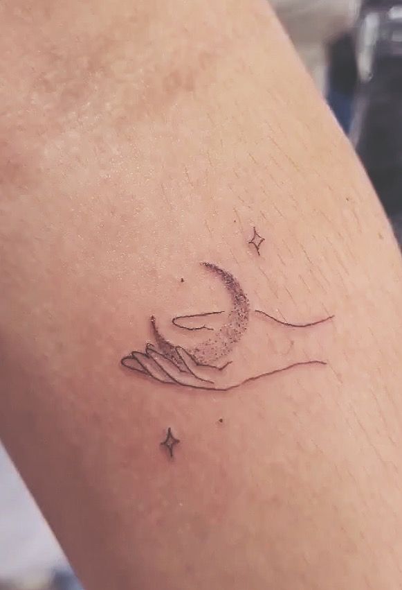 a woman's arm with a small tattoo on it that has a crescent moon and stars