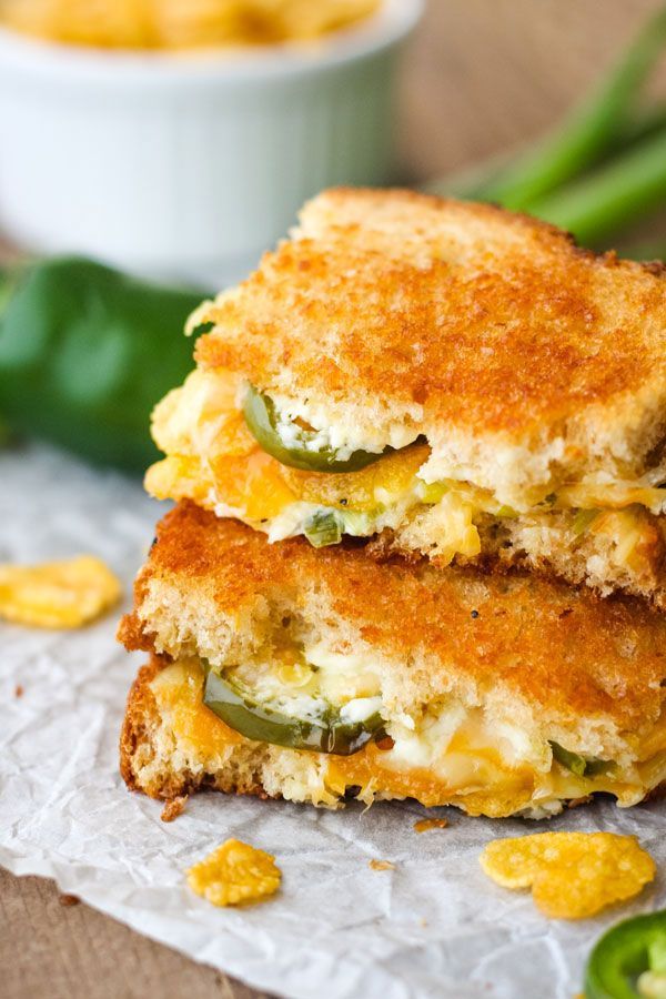 two grilled cheese sandwiches stacked on top of each other with green peppers and jalapenos in the background