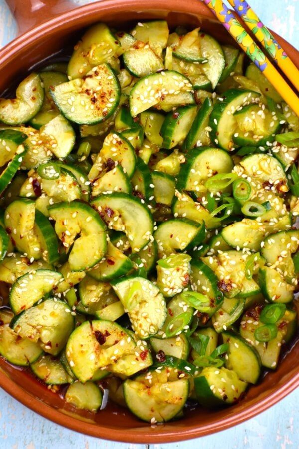 a brown bowl filled with sliced cucumbers and sesame seeds next to chopsticks