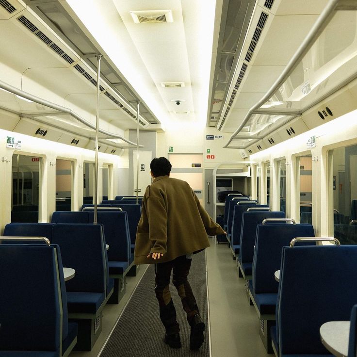 a man walking down a long hallway on a subway train with blue seats around him