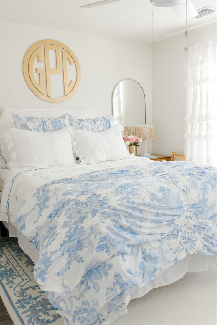 a white and blue bed in a bedroom next to a window with a mirror on the wall