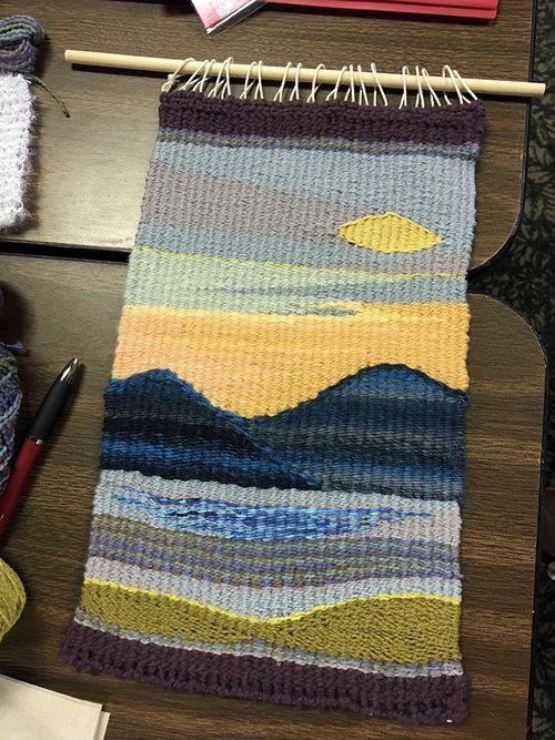 a knitted rug sitting on top of a wooden table next to yarn and knitting needles