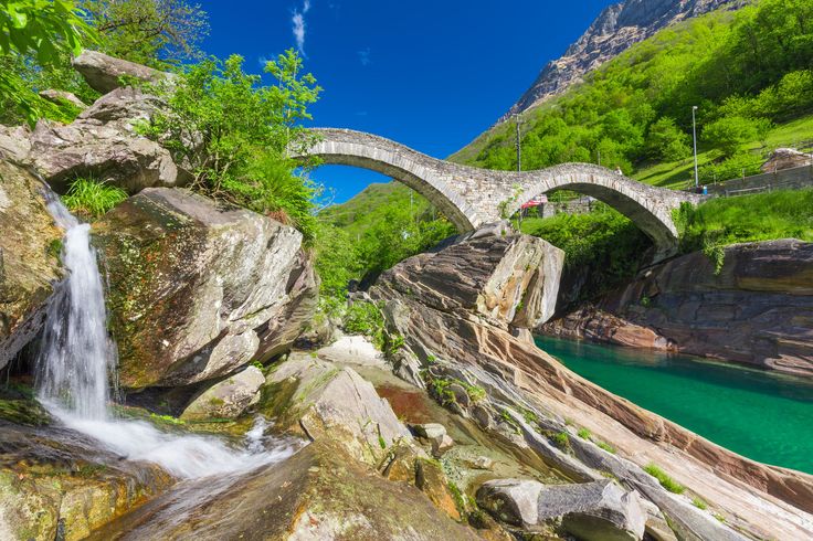 a stone bridge over a river next to a lush green hillside