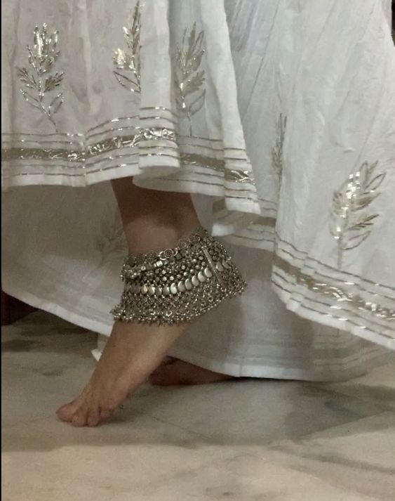 a woman's feet with silver beaded barefoot sandals on top of her legs