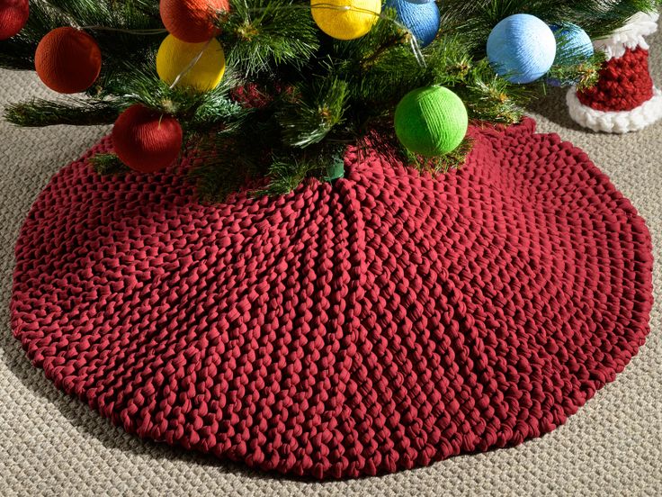 a knitted christmas tree skirt on the floor with ornaments around it and santa's hats in the background