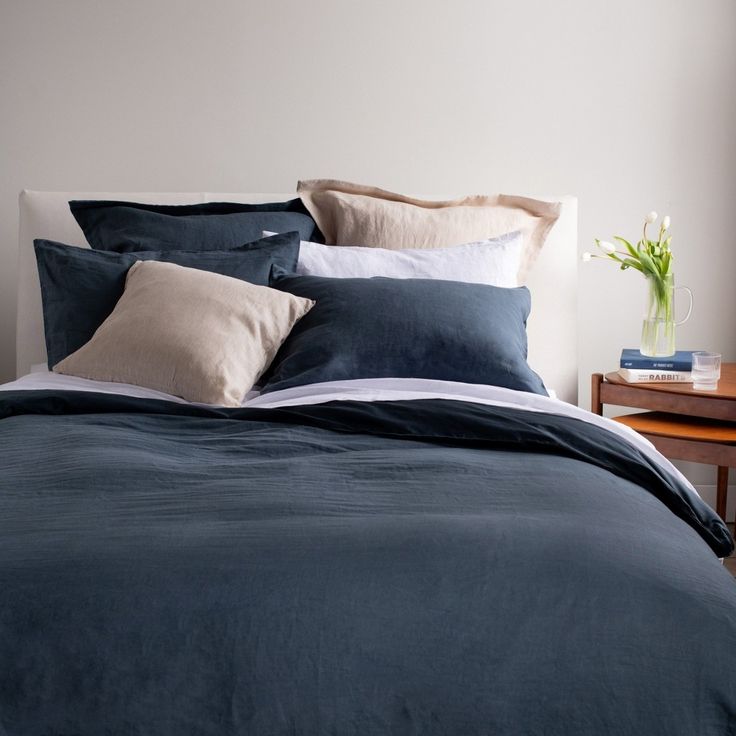 a bed with blue sheets and pillows on top of it next to a wooden night stand