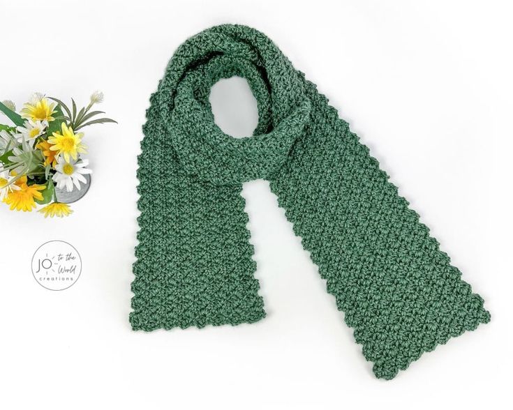 a green crocheted scarf next to a vase with yellow flowers on the side