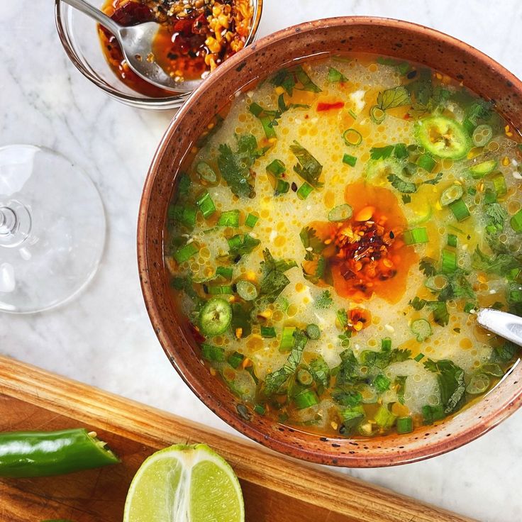 a bowl of soup on a table next to two wine glasses and a cutting board