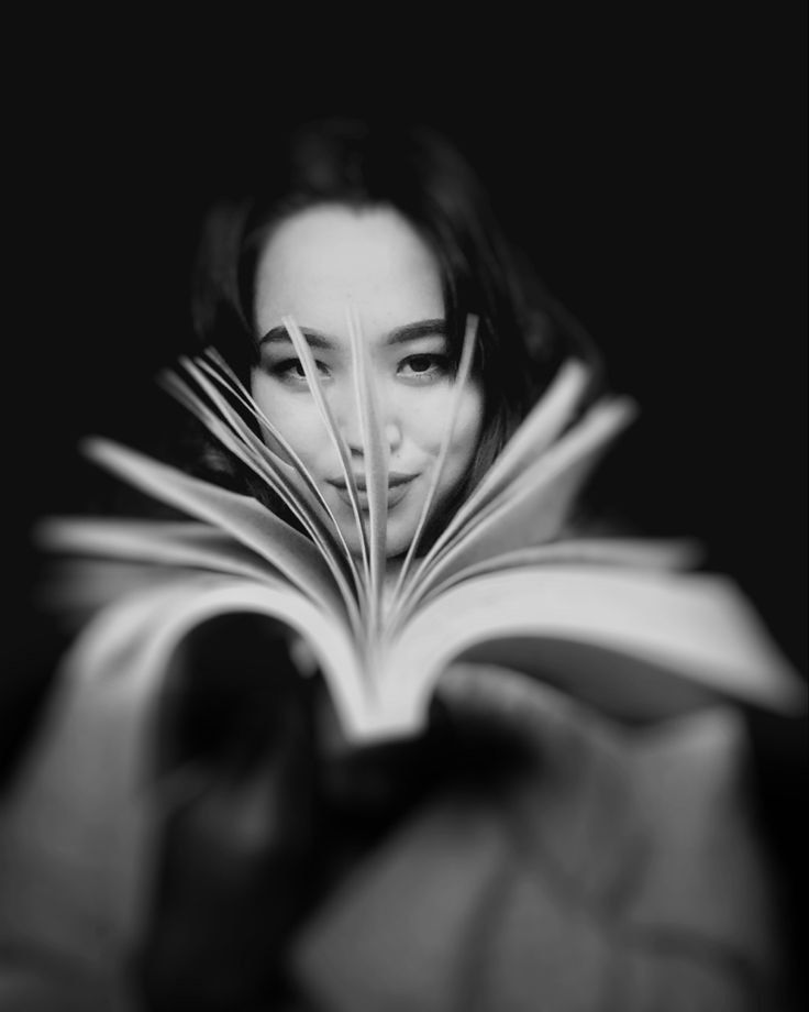 a woman is reading a book with her face hidden by the pages in black and white