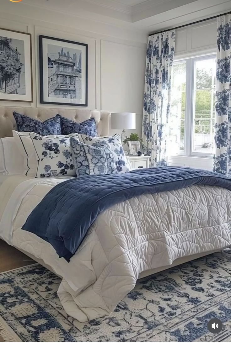 a bed with blue and white comforter in a bedroom next to a window filled with curtains