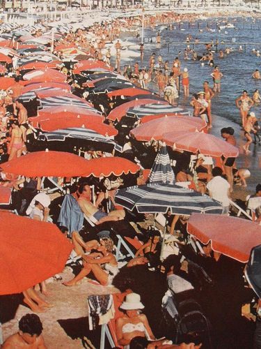 many people are on the beach with red umbrellas