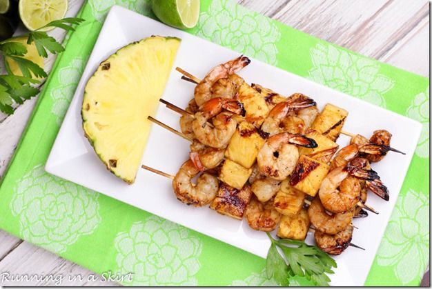 grilled shrimp and pineapple skewers on a white plate with a lime wedge