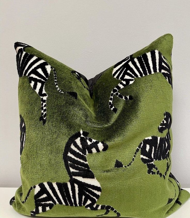 a green pillow with zebras on it sitting on top of a white table next to a wall