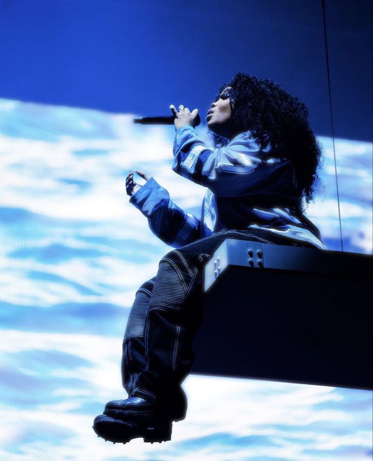 a woman with long black hair sitting on top of a bench while holding a microphone