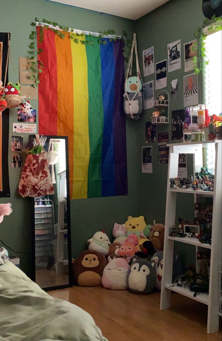 a bedroom with a rainbow flag hanging from the wall and stuffed animals on the floor