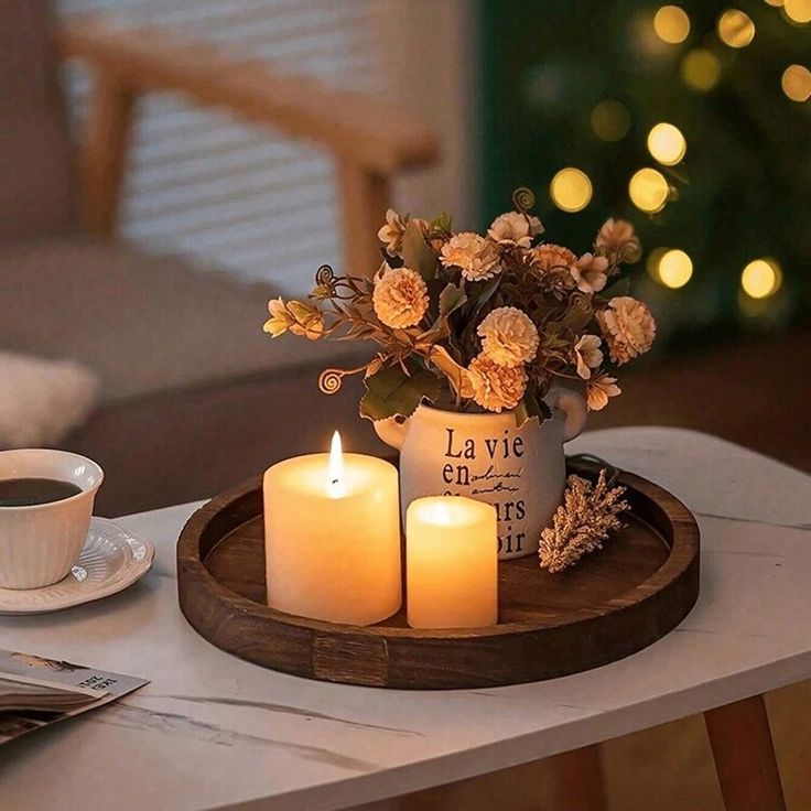 two lit candles on a tray with flowers and a cup of coffee next to it