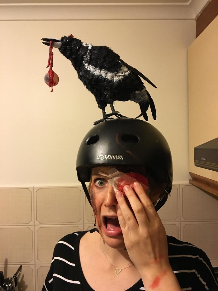 a woman wearing a helmet with a bird on top of her head and an apple in front of her face