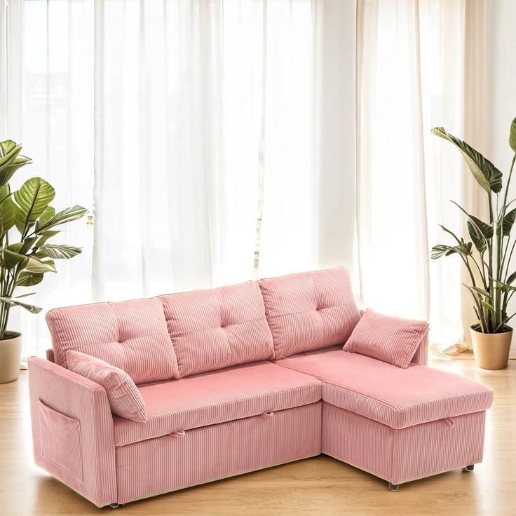 a pink couch sitting in front of a window next to a potted plant