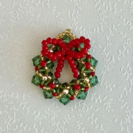 a red and green beaded christmas wreath ornament on a white tablecloth