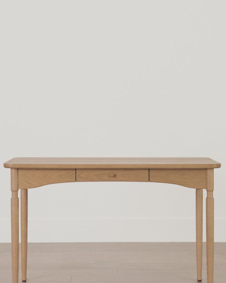 a wooden table sitting on top of a hard wood floor next to a white wall