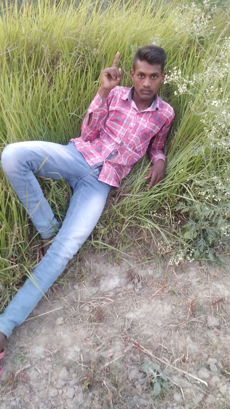 a man laying on the ground in front of some tall grass with his fingers up