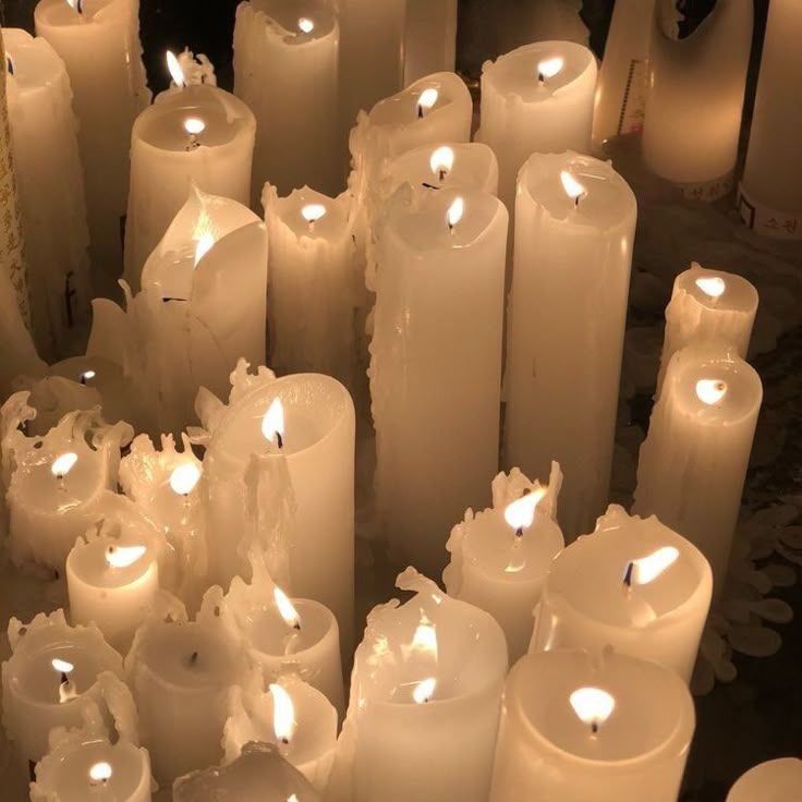 many lit candles are arranged in rows on the floor, with one being surrounded by smaller ones