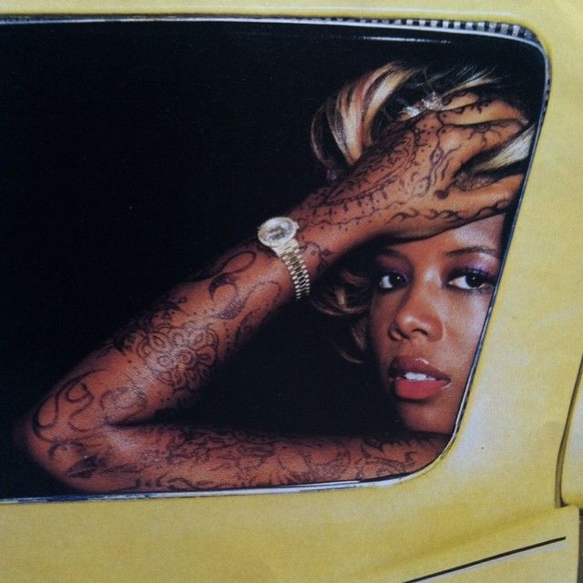 a woman with tattoos on her arm looking out the window of a yellow car while holding her hand up to her head