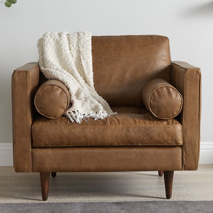 a brown leather chair with a white blanket on it's back and legs, in front of a white wall