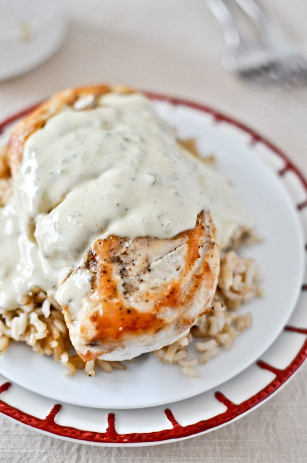 a white plate topped with chicken covered in gravy next to rice on a table