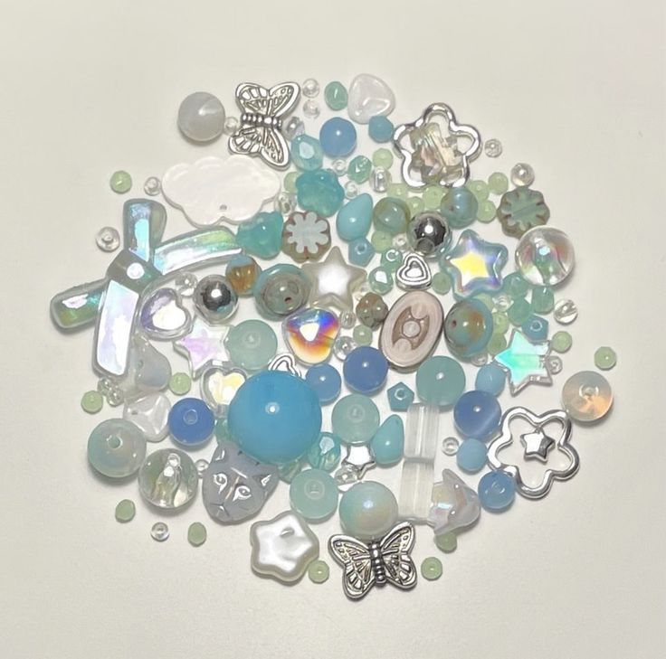 a bunch of glass beads and charms on a white surface with a butterfly in the middle