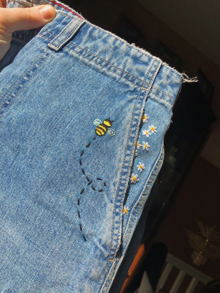 someone is holding up a jean skirt with a bee embroidered on the front and side