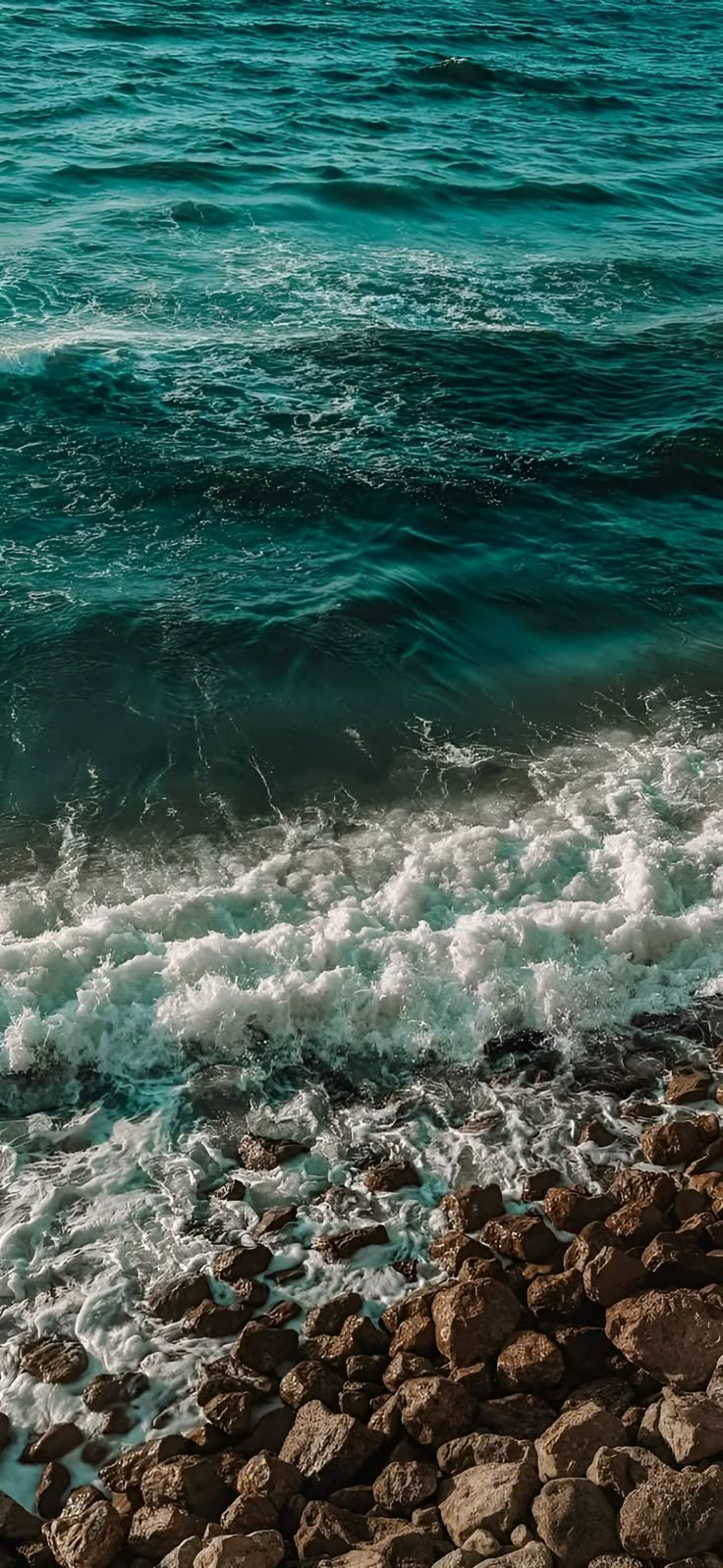 the water is blue and green with waves coming in from the rocks on the shore