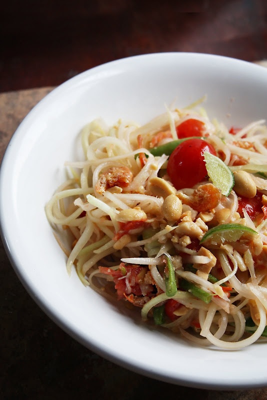 a white bowl filled with pasta and vegetables on top of a wooden table next to a fork