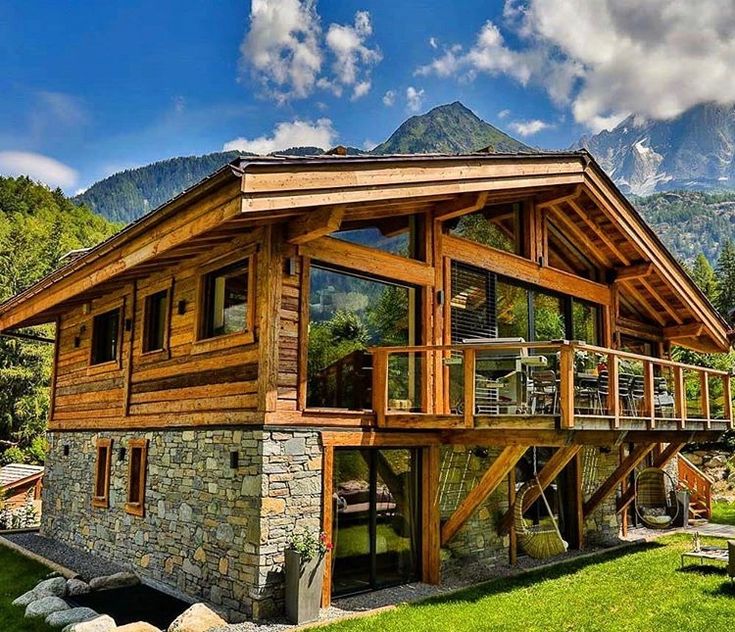 a large wooden house sitting in the middle of a lush green field next to mountains