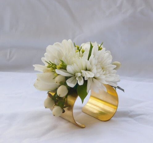 a bouquet of white flowers in a gold vase on a white cloth covered tablecloth