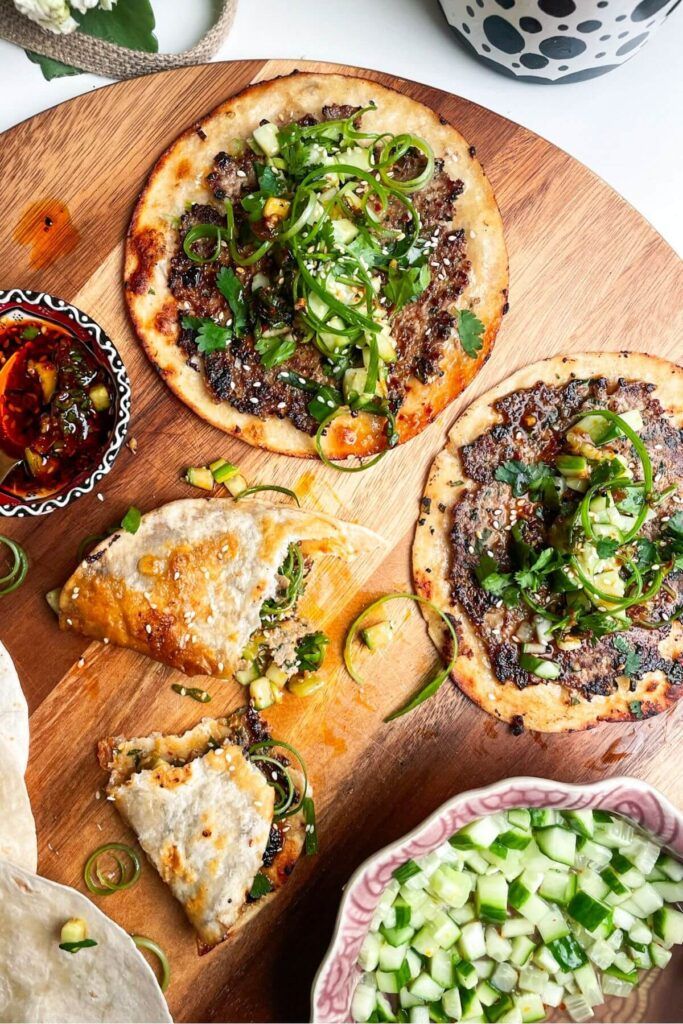 three small pizzas with toppings on a cutting board next to bowls of vegetables